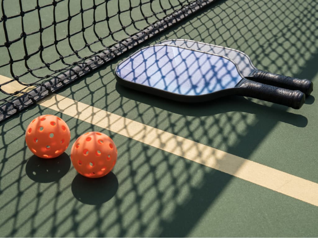 This is a photo of a pickleball court serving racket, and balls laid out on a pickleball court